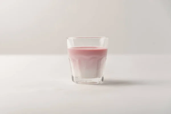 Стекло с розовым сиропом в молоке на белом фоне — стоковое фото