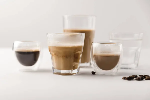 Verres avec assortiment de boissons au café sur fond blanc avec grains de café — Photo de stock