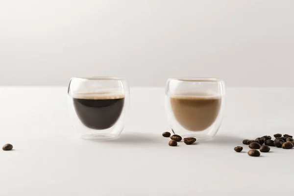 Две чашки с кофе на белом фоне с кофейными зёрнами — стоковое фото