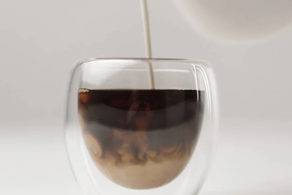 Verter leche en taza con café sobre fondo blanco - foto de stock