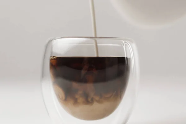 Pouring milk to cup with coffee on white background — Stock Photo