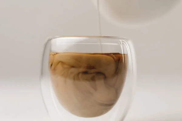 Añadir leche a la taza con café sobre fondo blanco - foto de stock