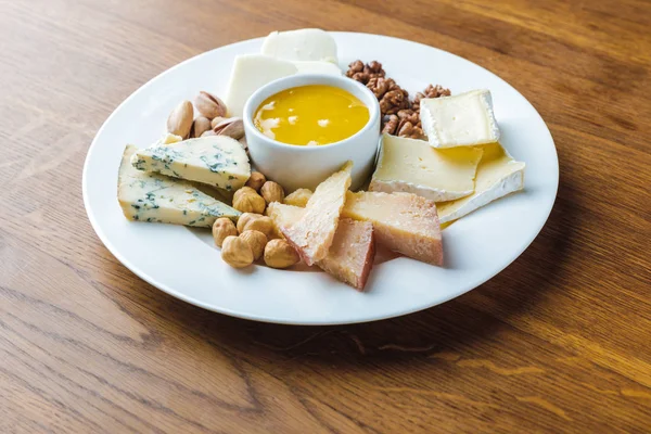 Close-up view of delicious cheese plate with nuts and honey on wooden tabletop — Stock Photo