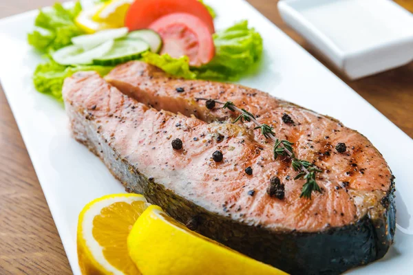 Vue rapprochée du saumon rôti gastronomique avec tranches de citron et salade de légumes — Photo de stock