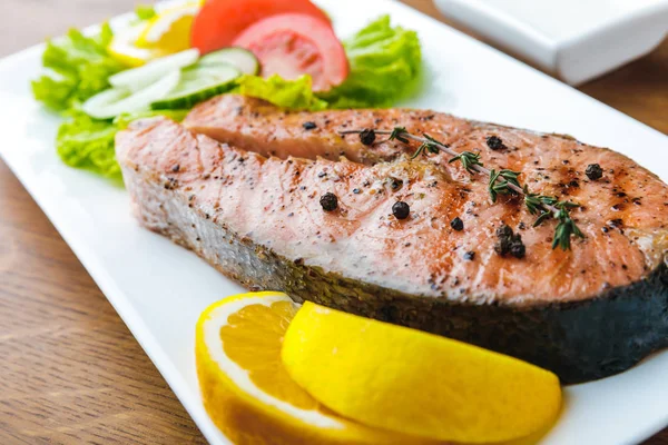 Крупный план вкусного лосося на гриле с ломтиками лимона и овощным салатом — стоковое фото