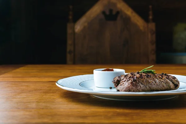 Delicious grilled steak with rosemary and bbq sauce on plate on wooden table — Stock Photo