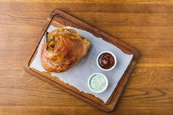 Blick von oben auf Gourmet-gebratene Schweinshaxe mit Soßen auf Holztischplatte — Stockfoto