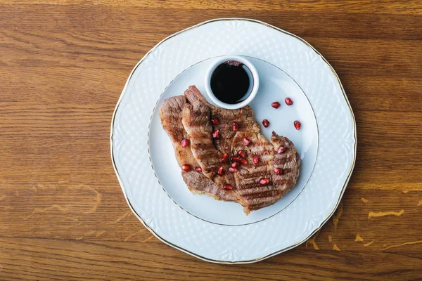 Top view of delicious grilled steaks with pomegranate seeds and sauce on wooden tabletop — Stock Photo