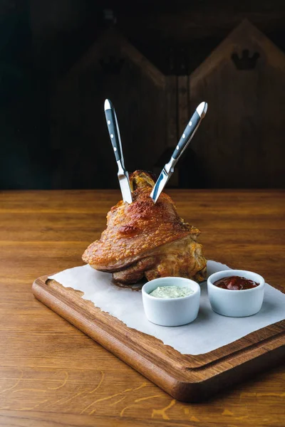 Jarret de porc rôti avec couteaux et sauces sur plateau en bois — Photo de stock