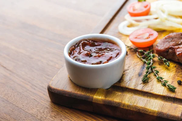 Close-up view of bbq sauce and roasted meat with vegetables on wooden board — Stock Photo