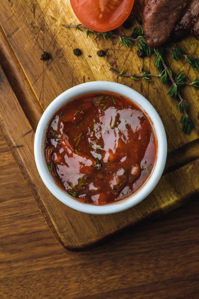 Vista superior de molho de churrasco na tigela e deliciosa carne assada com tomate na tábua de madeira — Stock Photo