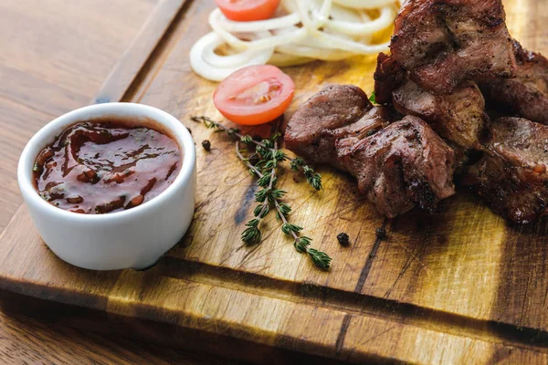 Close-up view of grilled meat with vegetables and bbq sauce on wooden board — Stock Photo