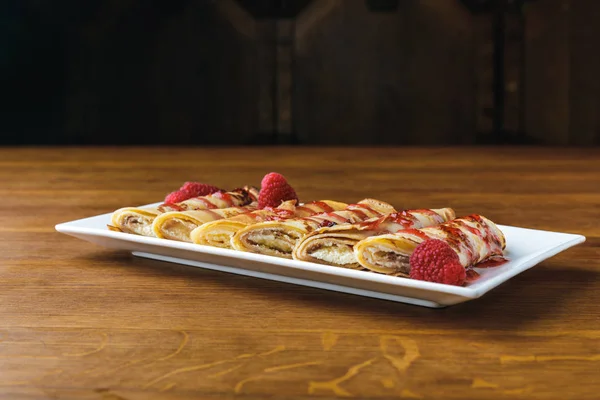 Sweet gourmet rolled pancakes with raspberries and syrup — Stock Photo