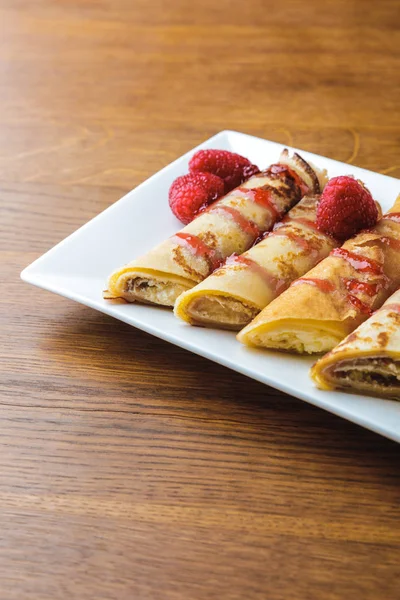 Delicious sweet rolled pancakes with raspberries and jam — Stock Photo