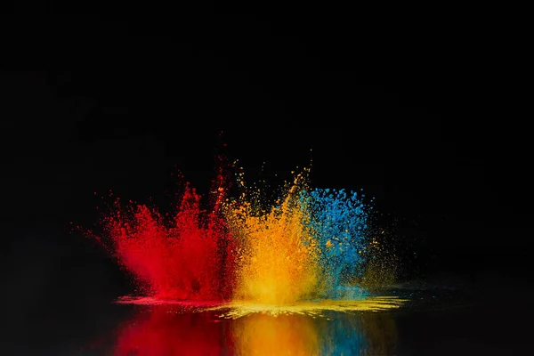 Red, blue and yellow holi powder explosion on black, Hindu spring festival — Stock Photo