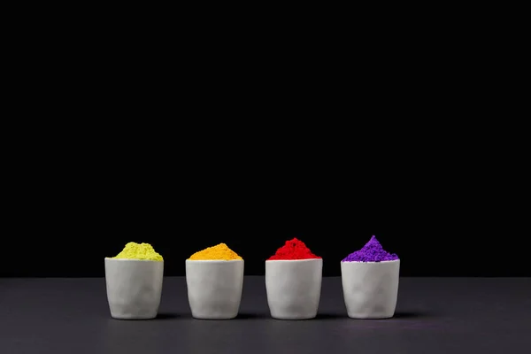 Row of colorful holi paint in four bowls on black, Hindu spring festival — Stock Photo