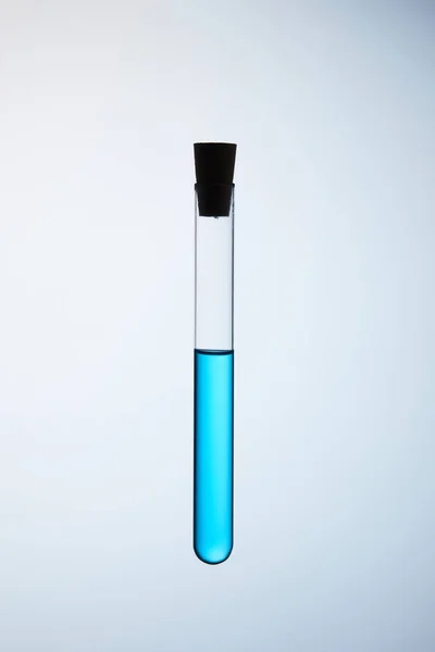 Tubo de ensayo lleno de líquido azul flotando en el aire sobre gris - foto de stock