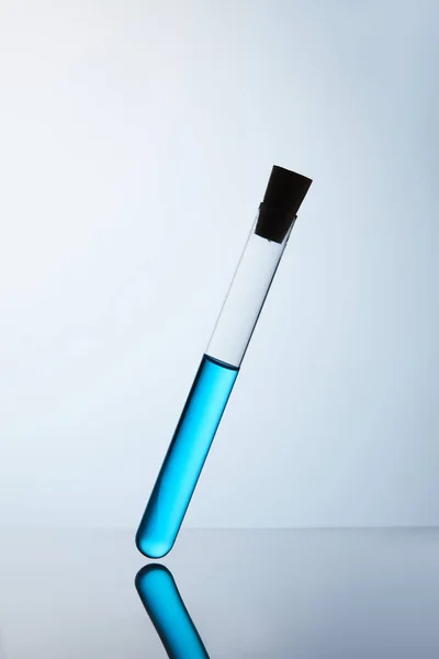 Tubo chimico riempito con liquido blu su superficie riflettente — Foto stock