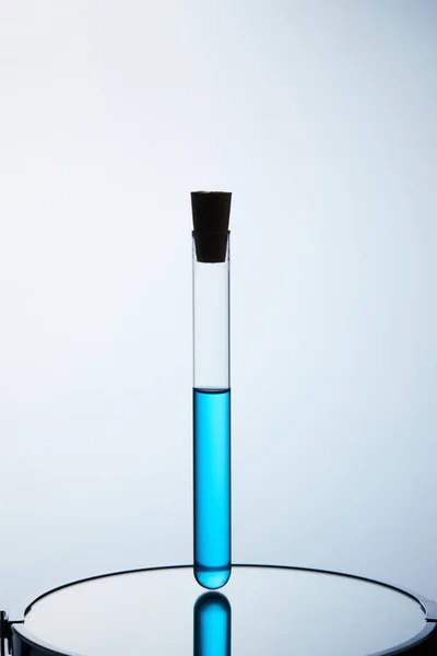 Пробирка заполнена синей жидкостью, стоящей на отражающей поверхности — стоковое фото