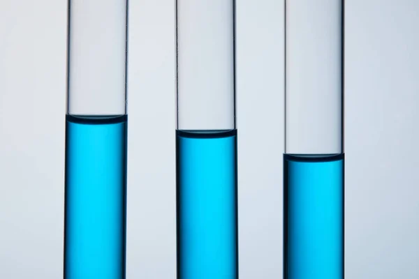 Close-up shot of test tubes filled with blue liquid in row on grey — Stock Photo