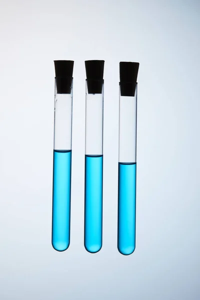 Zusammensetzung der mit blauer Flüssigkeit gefüllten Reagenzgläser, die in der Luft auf grau schweben — Stockfoto