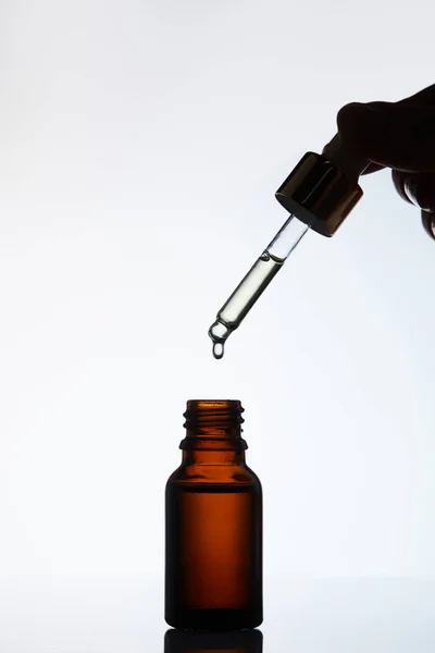 Recortado tiro de mujer dejando caer aceite en botella de la pipeta en blanco - foto de stock