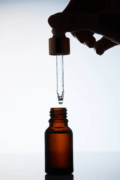 Cropped shot of woman dropping aromatic oil into bottle from pipette on white — Stock Photo