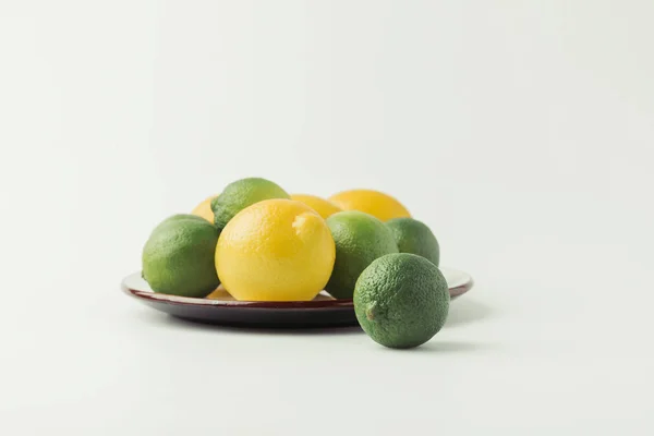 Lemons and limes on plate isolated on white background — Stock Photo