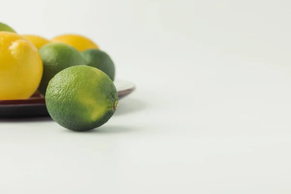 Limoni verdi e limoni su piatto su fondo bianco — Foto stock