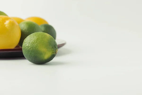 Green limes and lemons on plate on white background — Stock Photo