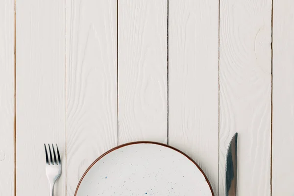 Leerer Teller mit Gabel und Messer auf weißem Holzgrund — Stockfoto