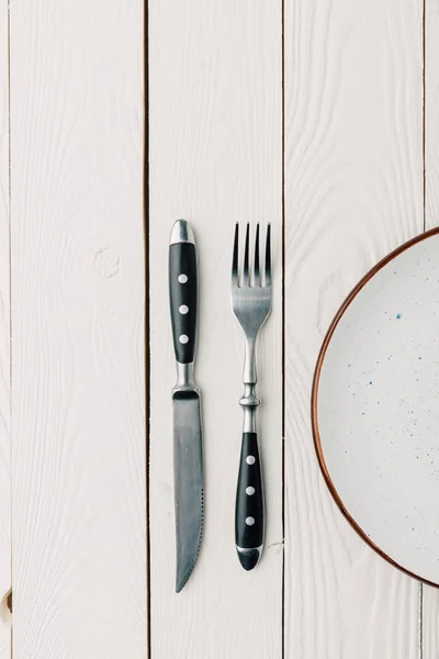 Draufsicht auf leeren Teller und Tafelbesteck auf weißem Holzgrund — Stockfoto