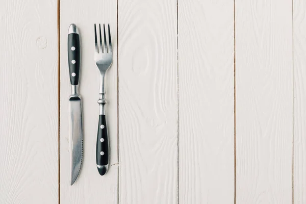 Vue du dessus de la fourchette et du couteau sur fond blanc en bois — Photo de stock