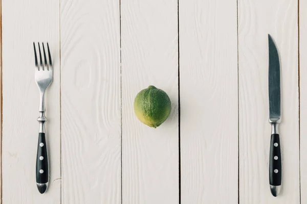 Верхний вид столовых приборов и зеленой извести на белом деревянном фоне — стоковое фото