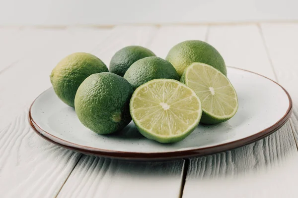 Green limes on plate on white wooden background — Stock Photo