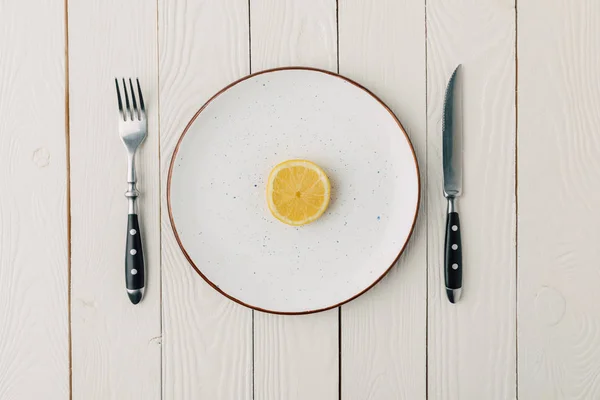 Half of juicy lemon on plate with cutlery on white wooden background — Stock Photo