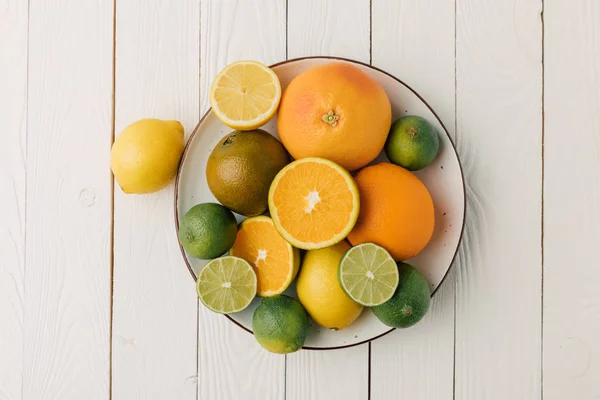 Juicy sour citruses on plate on white wooden background — Stock Photo