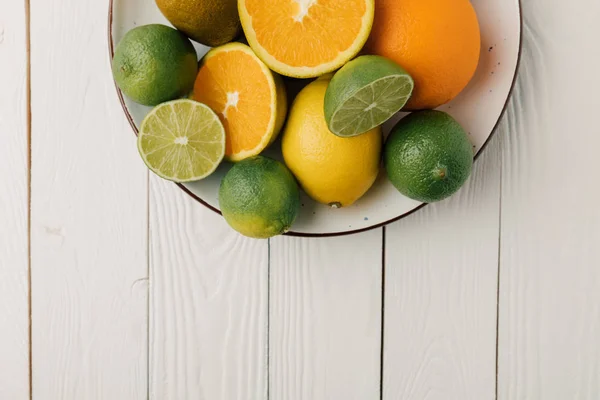 Frutas cítricas no prato em fundo de madeira branca — Fotografia de Stock