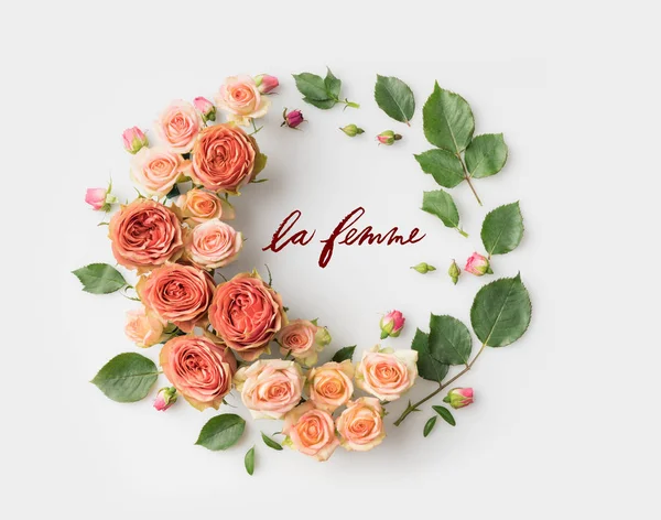 Letrero LE FEMME rodeado de corona de flores rosadas con hojas, brotes y pétalos aislados en blanco - foto de stock