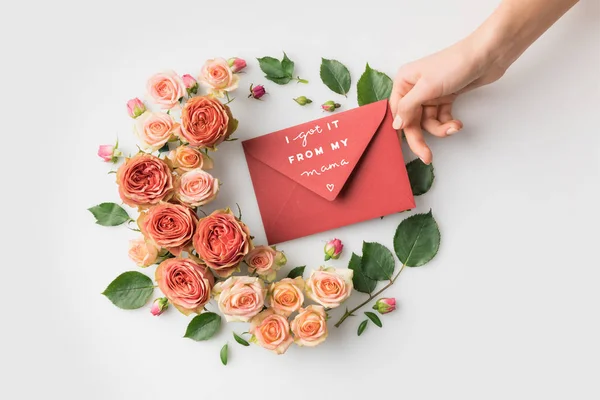 Mão segurando envelope com mães dia saudação cercada por belas flores rosa isolado no branco — Fotografia de Stock