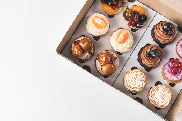 Vue de dessus des cupcakes savoureux arrangés dans la boîte en carton isolé sur blanc — Photo de stock