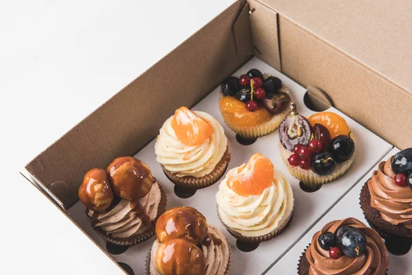 Vista de perto de vários tipos de cupcakes em caixa de papelão isolado em branco — Fotografia de Stock