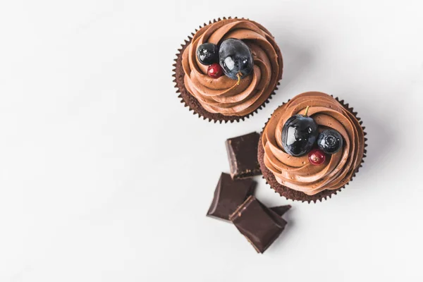 Top view of chocolate cupcakes with cream, grape, berries and pieces of chocolate isolated on white — Stock Photo