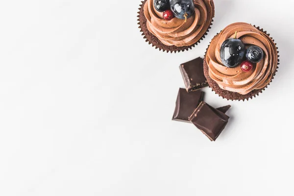 Vue du dessus de cupcakes au chocolat avec crème, raisin, baies et morceaux de chocolat isolés sur blanc — Photo de stock