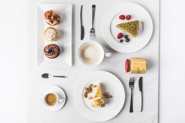 Вид сверху на расположение частей различных тортов на тарелках, чашки кофе и кексы изолированы на белом — стоковое фото