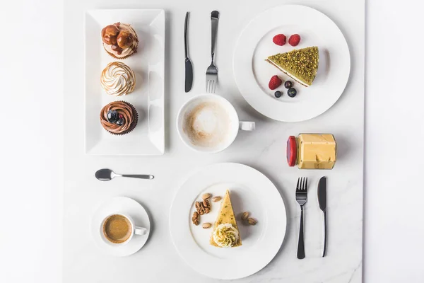 Top view of arrangement of pieces of various cakes on plates, cups of coffee and cupcakes isolated on white — Stock Photo