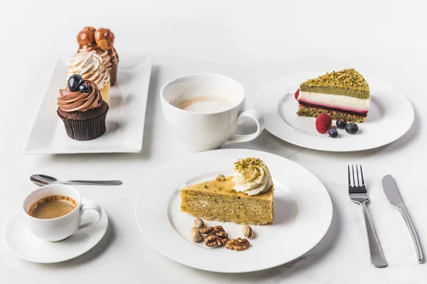 Close up view of arrangement of pieces of various cakes on plates, cups of coffee and cupcakes isolated on white — Stock Photo