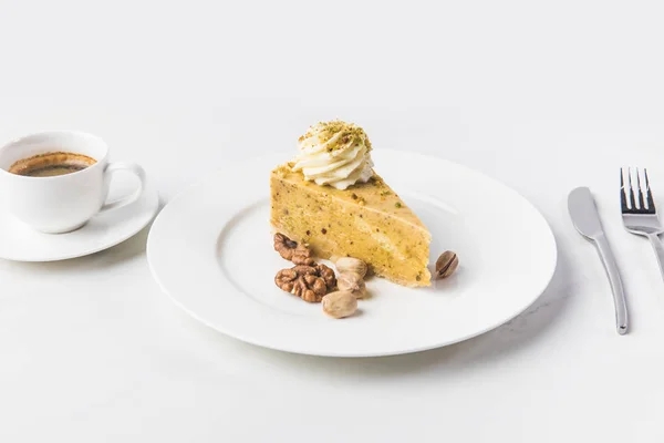 Vista de cerca del pedazo de pastel con nueces y taza de café aislado en la superficie blanca - foto de stock