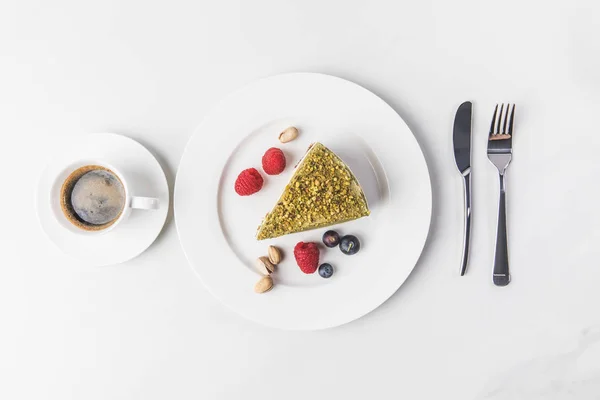 Blick von oben auf süßen Kuchen mit Pistazien und Beeren auf Teller und Tasse Kaffee isoliert auf weiß — Stockfoto