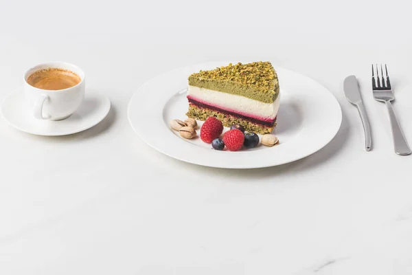 Vista da vicino torta dolce con pistacchi e bacche sul piatto e tazza di caffè isolato su bianco — Foto stock